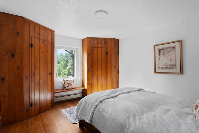 bedroom featuring a textured ceiling, baseboard heating, and light hardwood / wood-style flooring