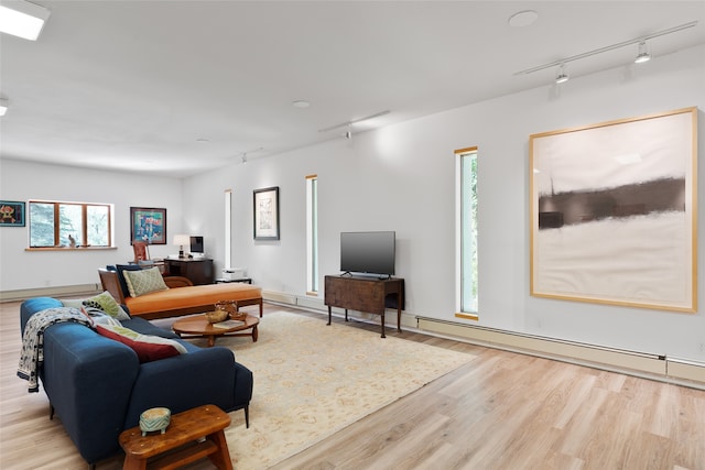 living room featuring a healthy amount of sunlight, baseboard heating, light hardwood / wood-style flooring, and track lighting