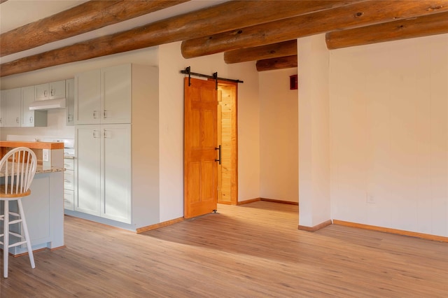 interior space with a barn door, beam ceiling, and light hardwood / wood-style flooring