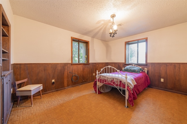 bedroom with a textured ceiling, wood walls, a chandelier, and light colored carpet