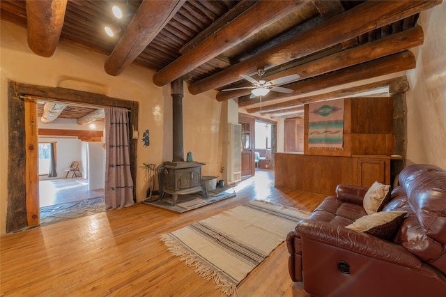 living room featuring light hardwood / wood-style floors, ceiling fan, beamed ceiling, and a wood stove