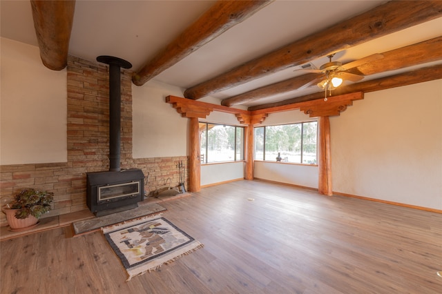 unfurnished living room with light wood-type flooring, ceiling fan, beamed ceiling, and a wood stove