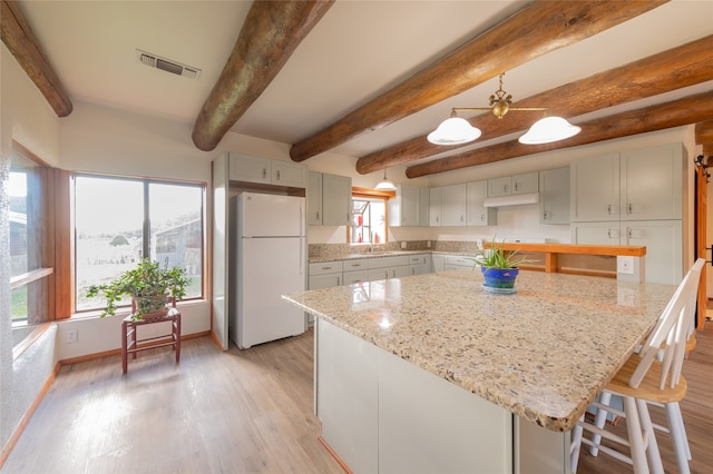 kitchen featuring beamed ceiling, white fridge, decorative light fixtures, a center island, and light hardwood / wood-style floors