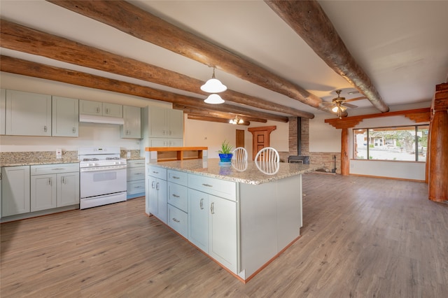 kitchen featuring white range, light hardwood / wood-style floors, a center island, a wood stove, and beam ceiling