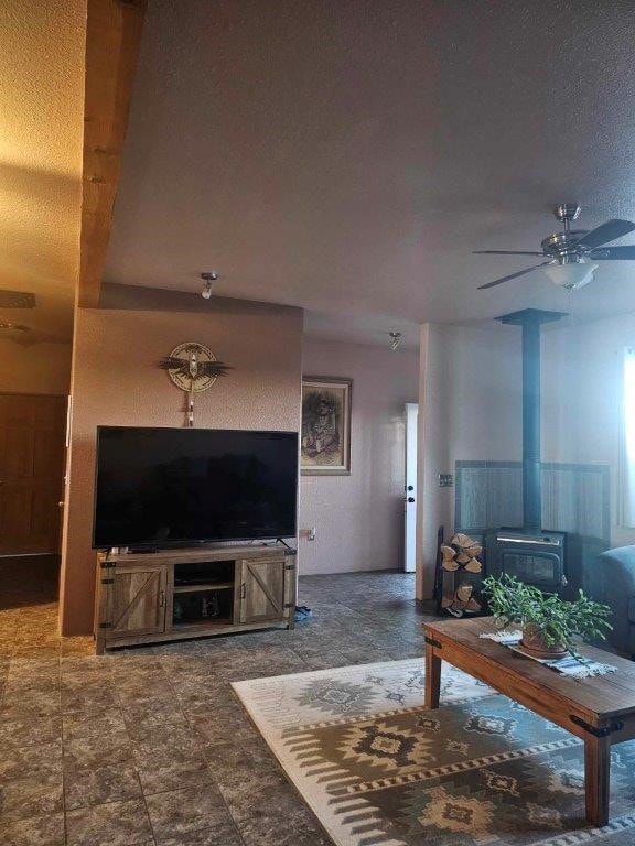 living room featuring a textured ceiling, a wood stove, ceiling fan, and beam ceiling