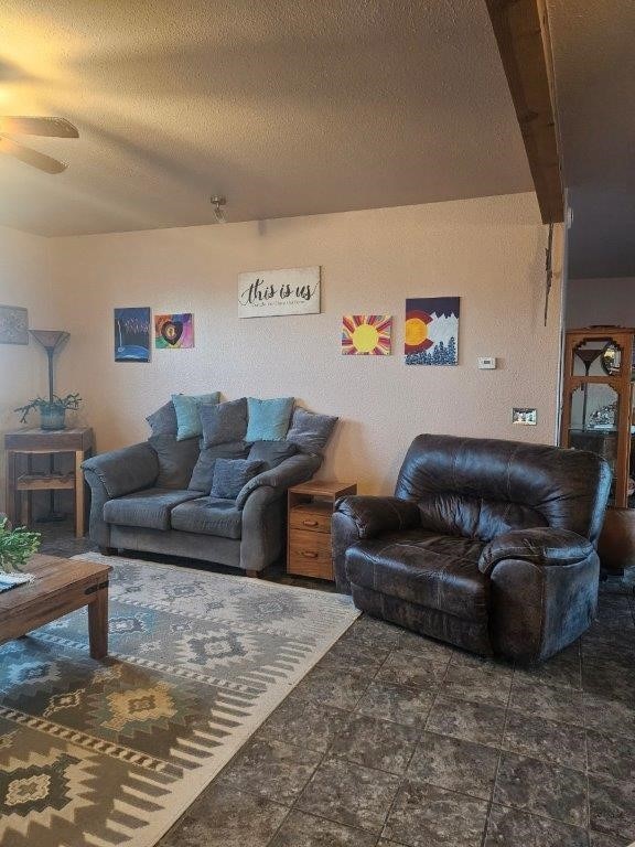 living room featuring beamed ceiling, ceiling fan, and a textured ceiling