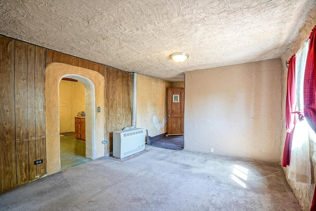 empty room featuring heating unit, wood walls, and carpet