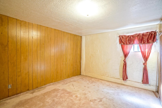 carpeted empty room featuring wooden walls and a textured ceiling