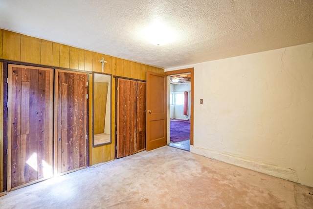 unfurnished bedroom featuring a textured ceiling, a closet, wooden walls, and light carpet