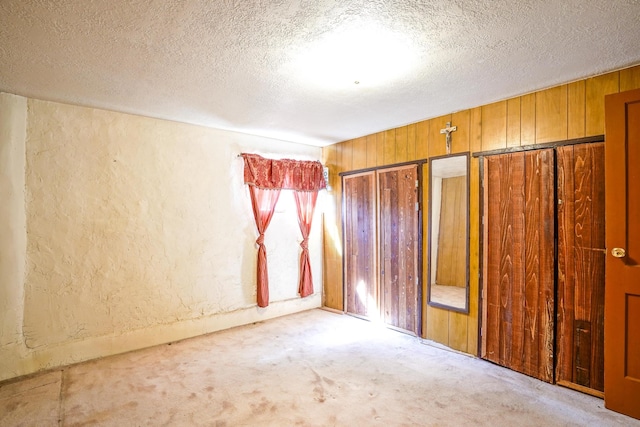 carpeted empty room featuring a textured ceiling and wood walls