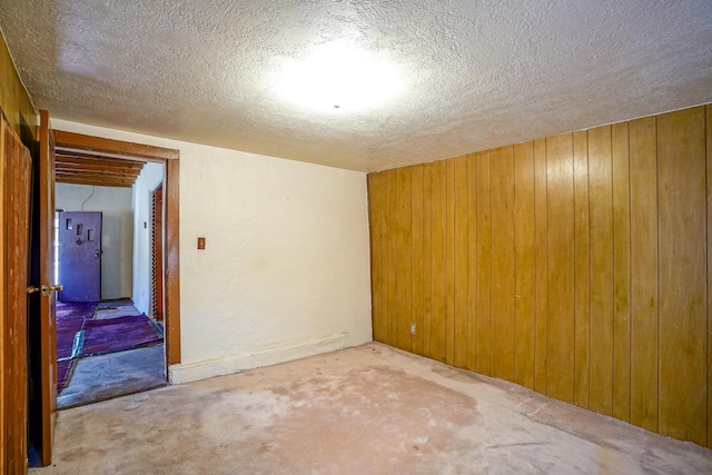 carpeted spare room with a textured ceiling and wooden walls