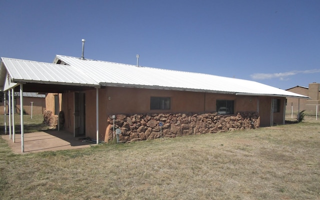 back of house featuring stucco siding, a lawn, and metal roof
