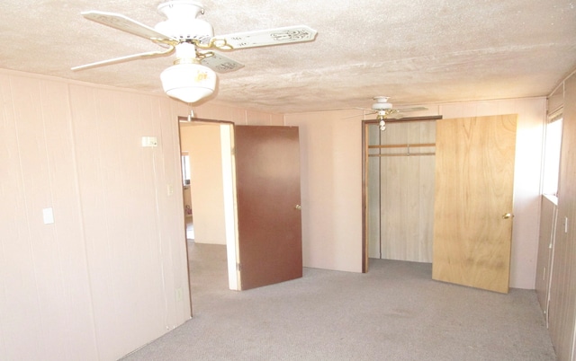 unfurnished bedroom with ceiling fan, light colored carpet, a closet, wooden walls, and a textured ceiling