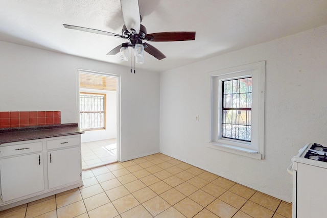 interior space featuring white cabinets, white stove, light tile patterned floors, and ceiling fan