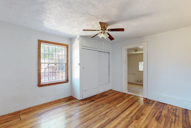 unfurnished bedroom featuring ceiling fan, a textured ceiling, a closet, and light hardwood / wood-style floors