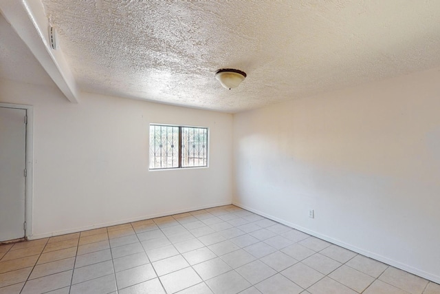 empty room with beamed ceiling, a textured ceiling, and light tile patterned floors