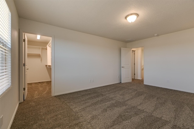 unfurnished bedroom with a walk in closet, a closet, dark carpet, and multiple windows