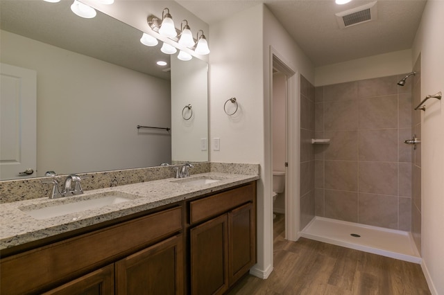 bathroom with toilet, a tile shower, hardwood / wood-style flooring, and vanity