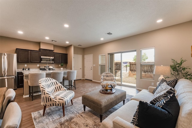 living room featuring light wood-type flooring, a textured ceiling, and sink