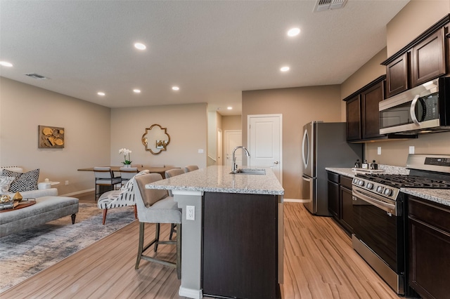 kitchen featuring appliances with stainless steel finishes, light hardwood / wood-style flooring, sink, a kitchen breakfast bar, and a center island with sink