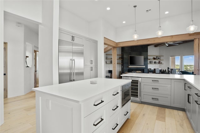 kitchen with gray cabinetry, hanging light fixtures, appliances with stainless steel finishes, a kitchen island, and light wood-type flooring