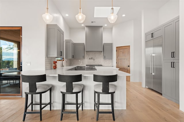 kitchen featuring pendant lighting, built in fridge, sink, wall chimney exhaust hood, and light wood-type flooring