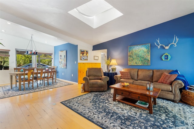 living room featuring hardwood / wood-style flooring, vaulted ceiling with skylight, and a chandelier