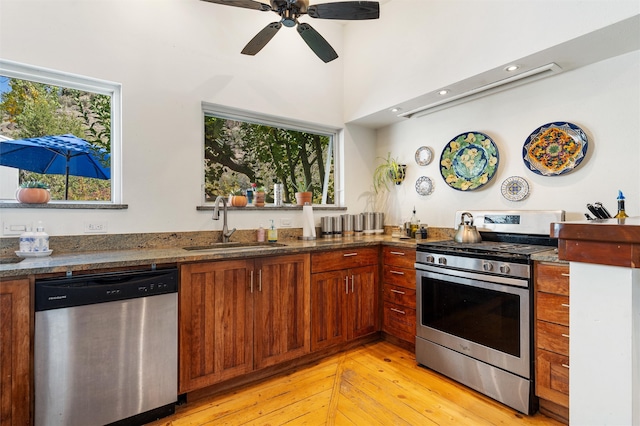 kitchen with ceiling fan, appliances with stainless steel finishes, light hardwood / wood-style flooring, dark stone countertops, and sink