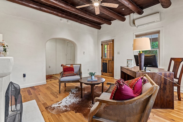 living room featuring light hardwood / wood-style floors, beam ceiling, an AC wall unit, and ceiling fan