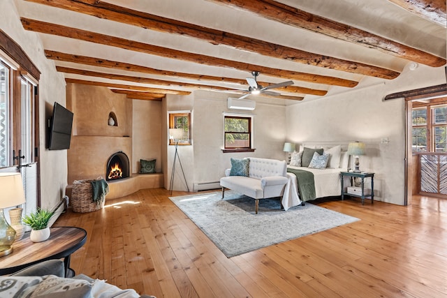 bedroom with light hardwood / wood-style floors, beam ceiling, a baseboard radiator, and a wall unit AC