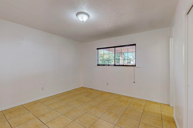 spare room with a textured ceiling, light tile patterned floors, and baseboards
