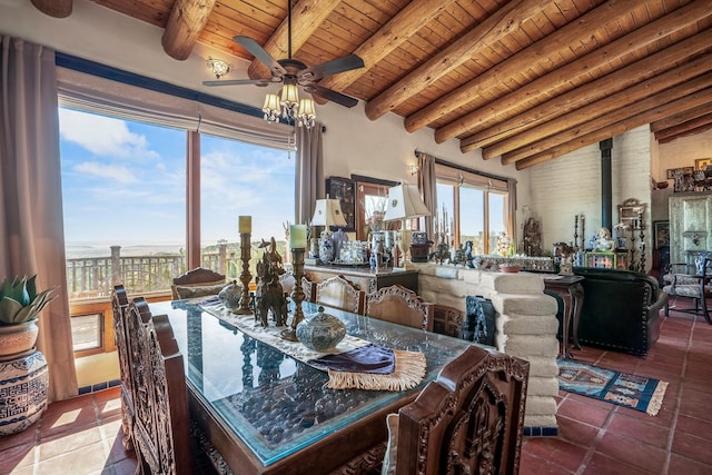 dining space with tile patterned floors, vaulted ceiling with beams, wood ceiling, a wood stove, and ceiling fan