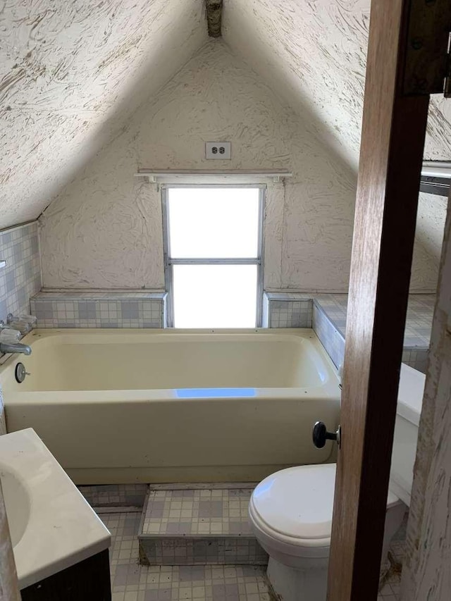 bathroom with vanity, toilet, a bathtub, and lofted ceiling