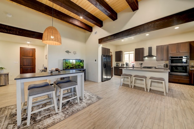 kitchen featuring wall chimney range hood, a kitchen island, a breakfast bar, light wood-type flooring, and stainless steel appliances