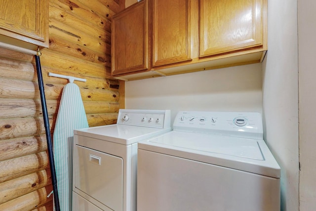 clothes washing area featuring cabinets, washer and clothes dryer, and log walls