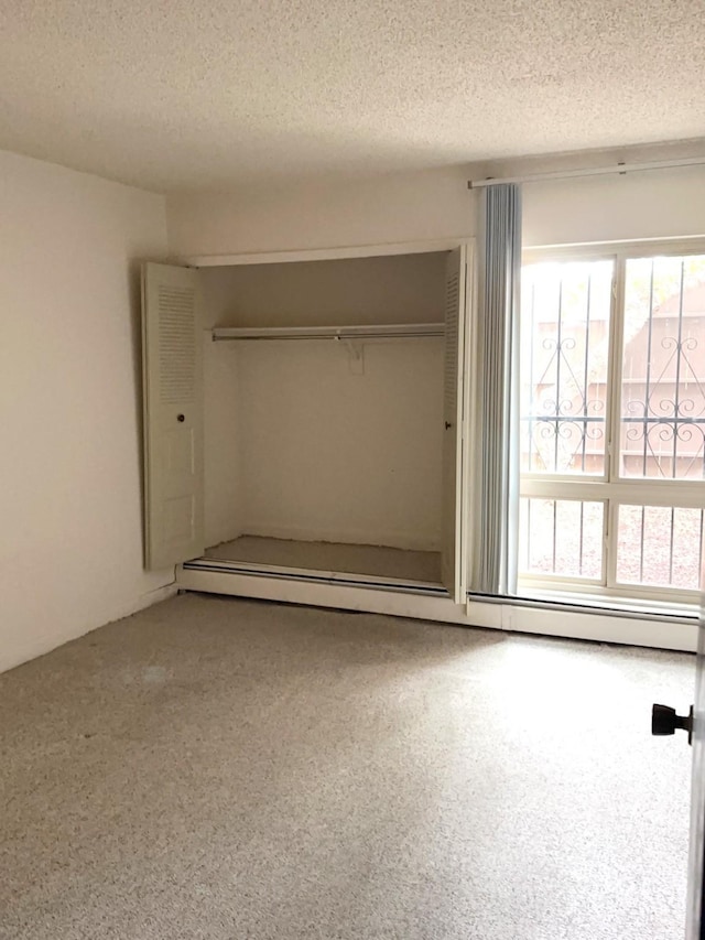 unfurnished bedroom featuring a textured ceiling, baseboard heating, and a closet