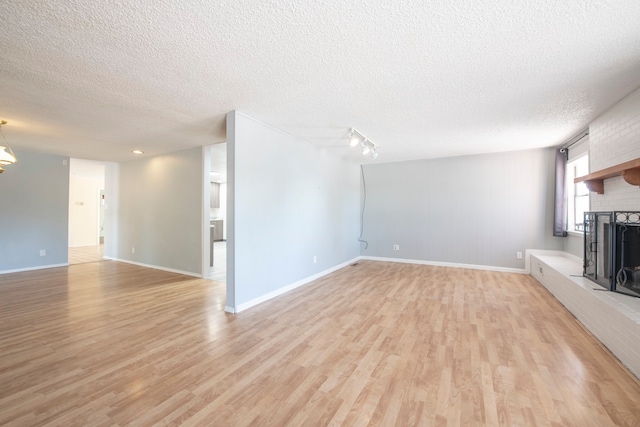 unfurnished living room featuring light hardwood / wood-style flooring, a textured ceiling, and a brick fireplace