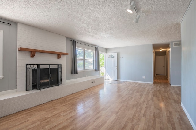 unfurnished living room featuring a textured ceiling, a brick fireplace, and light wood-type flooring