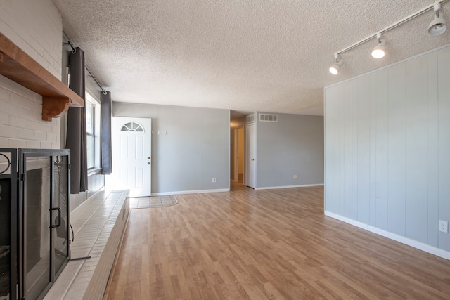 unfurnished living room with light hardwood / wood-style floors, a textured ceiling, track lighting, and a fireplace