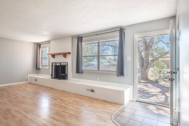 unfurnished living room with a wealth of natural light, light hardwood / wood-style flooring, a brick fireplace, and a textured ceiling