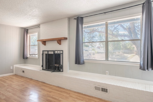 unfurnished living room featuring light hardwood / wood-style flooring, a textured ceiling, a fireplace, and a wealth of natural light