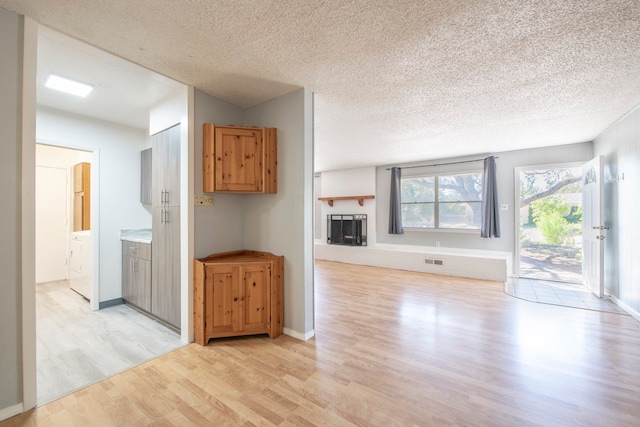 unfurnished living room featuring washer / clothes dryer, a textured ceiling, and light wood-type flooring