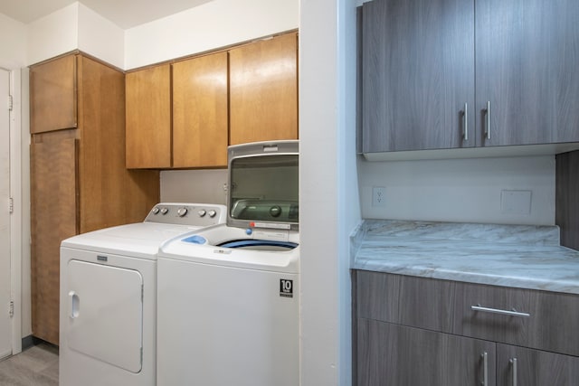 laundry area with light hardwood / wood-style flooring, washing machine and clothes dryer, and cabinets