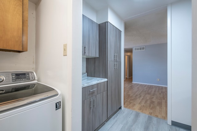 clothes washing area featuring washer / dryer, light hardwood / wood-style flooring, a textured ceiling, and cabinets