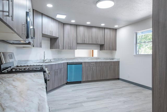 kitchen featuring appliances with stainless steel finishes, sink, light wood-type flooring, a textured ceiling, and light stone counters