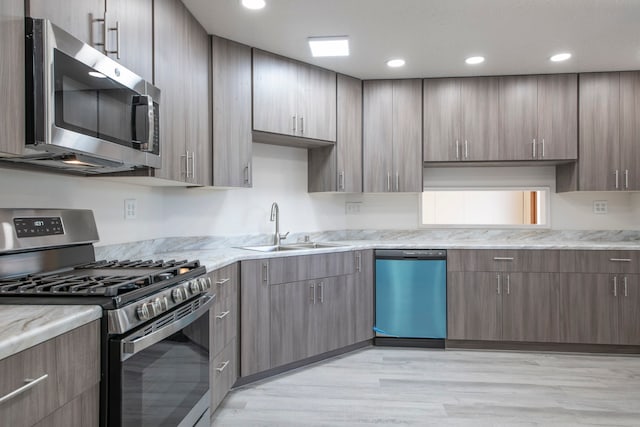 kitchen featuring sink, light stone counters, appliances with stainless steel finishes, and light hardwood / wood-style flooring