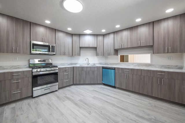 kitchen with a textured ceiling, stainless steel appliances, sink, and light wood-type flooring