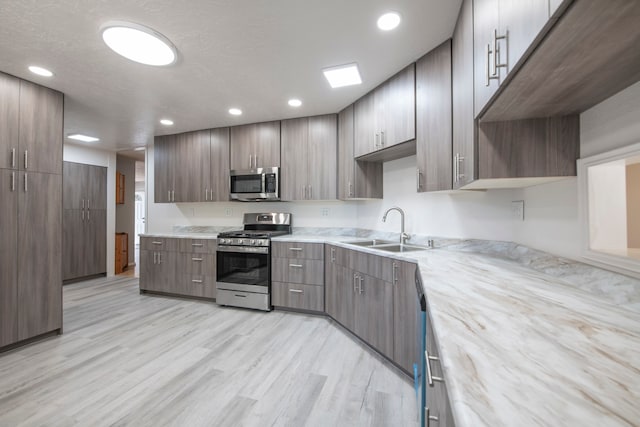 kitchen featuring sink, a textured ceiling, light hardwood / wood-style floors, stainless steel appliances, and light stone counters