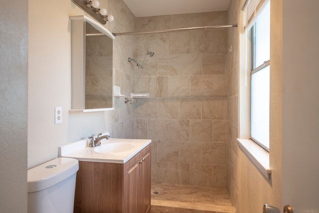 bathroom with vanity, toilet, a tile shower, and a wealth of natural light