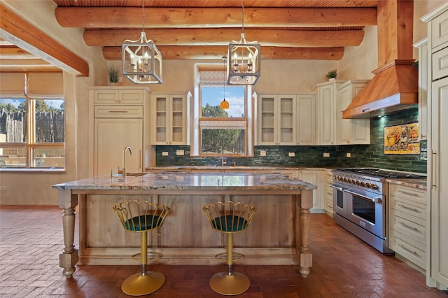 kitchen featuring beamed ceiling, a breakfast bar area, double oven range, light stone counters, and a center island with sink